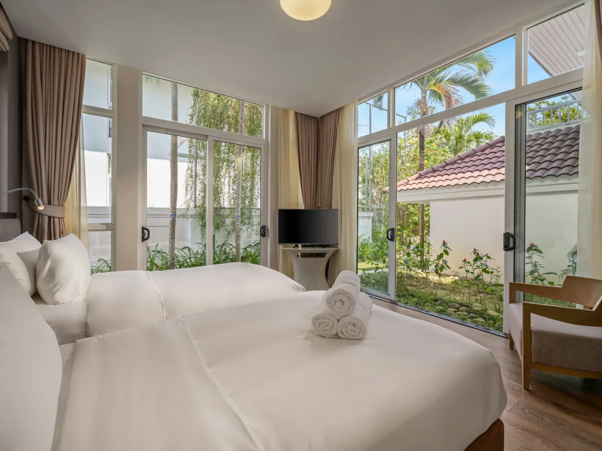 Giường trải ga trắng, khăn tắm gấp sẵn, cửa kính sát trần đón sáng